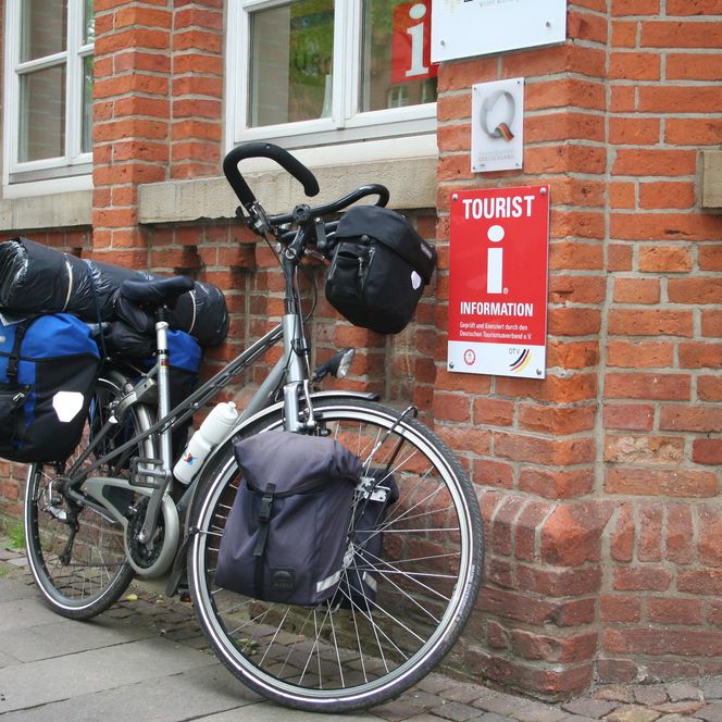 Ein bepacktes Fahrrad lehnt vor einem roten Ziegelgebäude der Tourist-Information Nienburg.