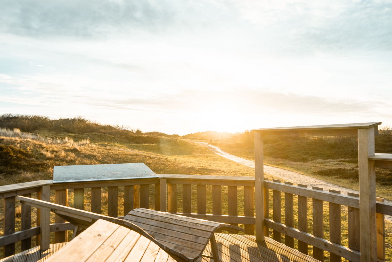 Holzplattform mit Bänken ragt in goldene Dünenlandschaft von Spiekeroog bei Sonnenuntergang.