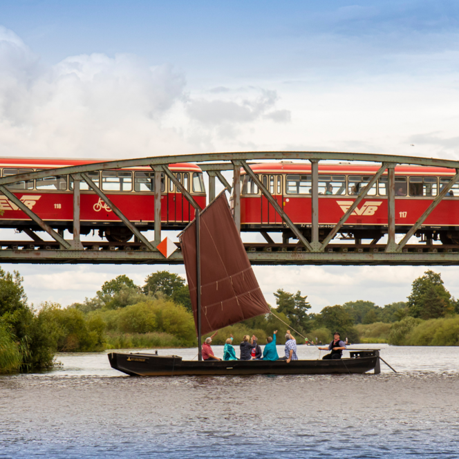 Ein Torfkahn fährt auf der Hamme vor der Eisenbahnbrücke, wo gerade der Moorexpress rüberfährt.