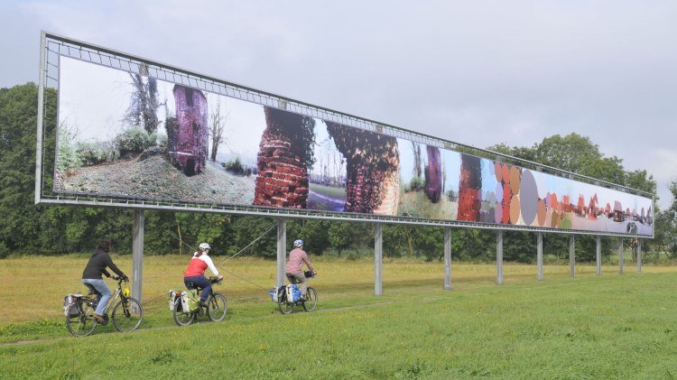 Three cyclists pass an art object, © TMN / Thorsten Brönner Three cyclists pass an art object, © TMN / Thorsten Brönner