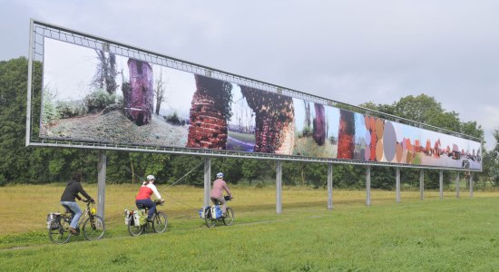 Three cyclists pass an art object, © TMN / Thorsten Brönner Three cyclists pass an art object, © TMN / Thorsten Brönner